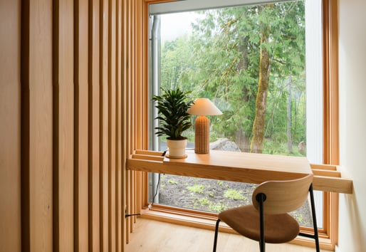 A desk that floats in front of a monumental picture window that begins at the floor and affords views of the forest outside.
