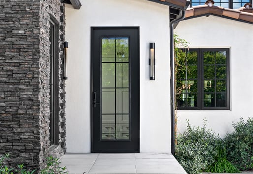 A Spanish-style entrance to a home with grey stone and white stucco walls and black windows and doors with colonial grilles.